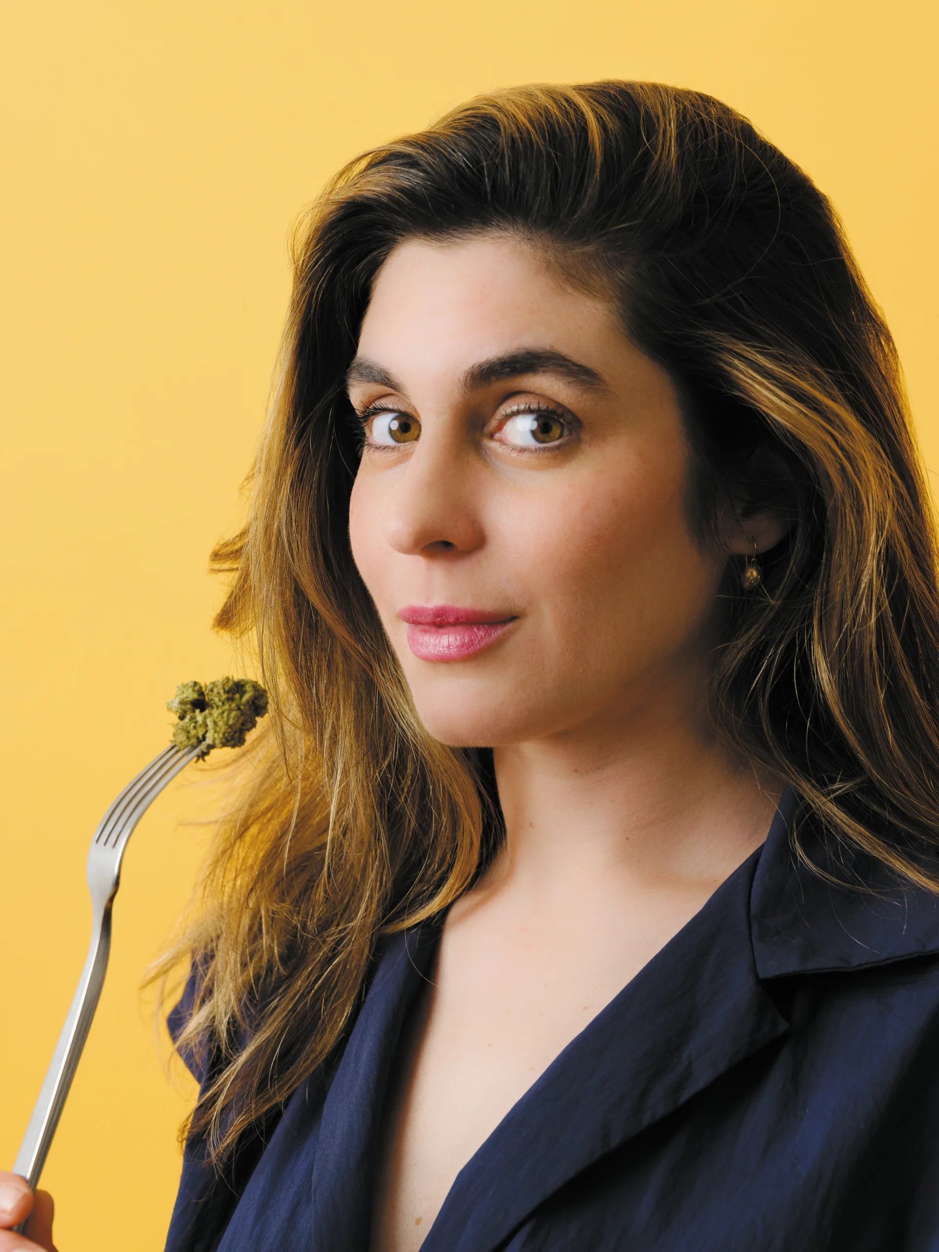 Portrait of Vanessa Lavorato holding a fork with a cannabis bud against a yellow background.