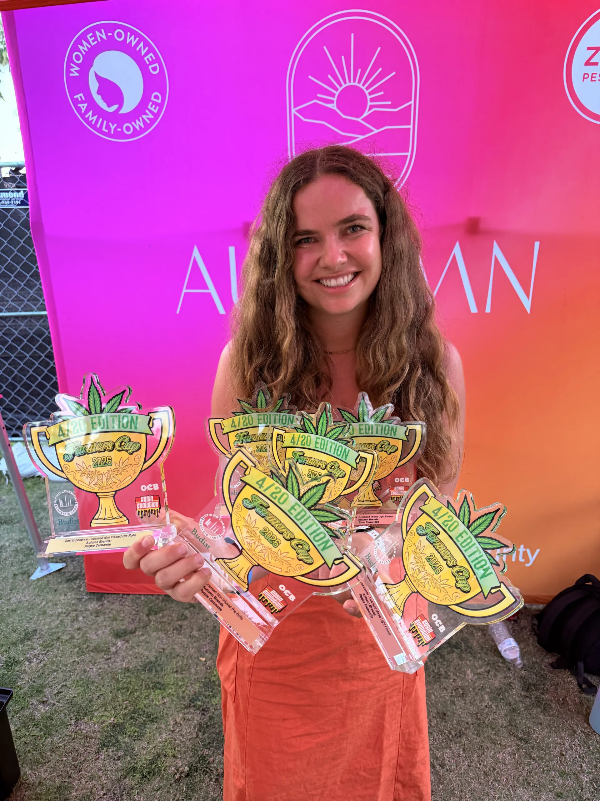 Hanna Brand of Autumn Brands holding seven Farmer's Cup 420 San Diego award trophies in front of the Autumn Brands booth after winning multiple awards for flower and prerolls, including Purple Carbonite and Sour Power #69. Award-Winning Cannabis